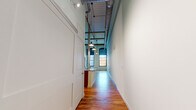 Located at 1241 College Ave SW in Lenoir, NC, this single-floor loft unit showcases a striking adaptive reuse design that preserves the raw industrial character of its origins while delivering contemporary comfort. Rich, wide-plank hardwood floors run throughout every room, lending warmth and continuity to the space. The main living area impresses with soaring ceilings, exposed ductwork, and large arched multi-pane windows that flood the room with abundant natural light and evoke the building's historic mill heritage. Original white-painted brick walls and structural columns add authenticity to the industrial aesthetic. The kitchen is well-appointed with warm wood cabinetry, granite countertops, a spacious island with a stainless steel sink, and a full suite of stainless steel appliances including a refrigerator, range, and microwave. The bedroom features impressively tall ceilings, two closets, and direct access to a private en-suite bathroom outfitted with a glass-enclosed tiled shower and a wood-vanity with a white countertop. A second bathroom provides a vanity and toilet, also finished with hardwood flooring. The overall ambiance is open, airy, and full of character — a seamless union of historic industrial design and modern living.
