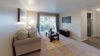This single-floor residence offers a thoughtfully designed layout with a warm, neutral color palette throughout. The expansive living room features plush carpeting, soft natural light, and sliding glass doors that open to a private outdoor patio, creating a seamless connection between indoor and outdoor living. Adjacent to the living area, the dining space is highlighted by a tray ceiling detail and an elegant chandelier overhead, with rich wood-look flooring that extends into the kitchen. The kitchen is outfitted with dark espresso cabinetry, light countertops, black appliances, and a window above the sink that brings in additional natural light. Two well-sized bedrooms each feature plush carpeting and windows that allow ample natural light. The primary bedroom includes a decorative iron-accented bed frame and classic wood nightstands, while the second bedroom offers generous floor space and a large window with outdoor views. The primary bathroom features dark wood cabinetry paired with light countertops and a tub-shower combination with wood-look flooring. A second bathroom provides additional built-in cabinetry storage and a stylish vessel-style sink. Together, the rooms offer a comfortable and cohesive living environment with practical storage solutions throughout.