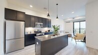 This contemporary 750 square foot apartment in Oakdale, MN, offers a harmonious blend of style and functionality. The open-concept design seamlessly integrates the kitchen and living areas, creating a spacious feel. The kitchen boasts sleek dark cabinetry, stainless steel appliances, and a generous island, perfect for meal prep and casual dining.

Both bedrooms are well-appointed, with the primary bedroom measuring 110 square feet. Large windows in the bedrooms provide ample natural light and scenic views. The two bathrooms feature modern fixtures, including a combination tub-shower, floating vanities, and stylish tile work.

The living area is adorned with comfortable seating and tasteful artwork, while sliding glass doors lead to a balcony, offering outdoor space and views. Light wood-look flooring runs throughout, complementing the crisp white walls and adding warmth to the space.

Practical amenities include in-unit laundry with stacked washer and dryer, ensuring convenience for residents. The apartment's thoughtful design maximizes the use of space, with clever storage solutions integrated throughout.

Located at 7600 2nd St N in Oakdale, this apartment combines urban comfort with a touch of nature, evident in the views from its windows. The modern finishes, functional layout, and attention to detail make this space an ideal home for those seeking contemporary living in a prime location.