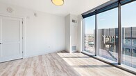 Located in the heart of downtown Austin at 501 Brazis St, this contemporary high-rise residence offers four bedrooms, two bathrooms, and a thoughtfully designed single-level layout. The open-concept living and kitchen area serves as the centerpiece of the home, where a sleek, elongated kitchen island with a white quartz countertop and undermount sink anchors the space. The kitchen features floor-to-ceiling cabinetry in a warm wood-tone finish, stainless steel appliances, a cooktop range, and track lighting overhead — all set against clean white walls and light wood-style flooring that runs throughout.

The living area transitions seamlessly toward dramatic floor-to-ceiling corner windows that frame sweeping panoramic views of the Austin skyline, flooding the space with natural light. Each bedroom continues the minimalist aesthetic, with the same light wood flooring, crisp white walls, and large-format windows offering impressive elevated city vistas. The primary bedroom provides a comfortable and well-proportioned retreat.

The bathrooms are finished with modern fixtures, including a soaking tub and shower combination adorned with large-format, dark stone-effect wall tiles and matte black hardware, paired with white cabinetry and quartz countertops. A dedicated hallway, entrance, and closet round out this well-appointed downtown residence.