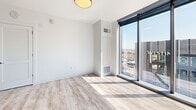 Located in the heart of downtown Austin at 501 Brazis St, this contemporary high-rise residence offers four bedrooms, two bathrooms, and a thoughtfully designed single-level layout. The open-concept living and kitchen area serves as the centerpiece of the home, where a sleek, elongated kitchen island with a white quartz countertop and undermount sink anchors the space. The kitchen features floor-to-ceiling cabinetry in a warm wood-tone finish, stainless steel appliances, a cooktop range, and track lighting overhead — all set against clean white walls and light wood-style flooring that runs throughout.

The living area transitions seamlessly toward dramatic floor-to-ceiling corner windows that frame sweeping panoramic views of the Austin skyline, flooding the space with natural light. Each bedroom continues the minimalist aesthetic, with the same light wood flooring, crisp white walls, and large-format windows offering impressive elevated city vistas. The primary bedroom provides a comfortable and well-proportioned retreat.

The bathrooms are finished with modern fixtures, including a soaking tub and shower combination adorned with large-format, dark stone-effect wall tiles and matte black hardware, paired with white cabinetry and quartz countertops. A dedicated hallway, entrance, and closet round out this well-appointed downtown residence.