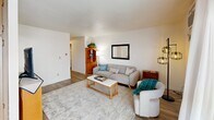 Located at 110 S Almon St in Moscow, Idaho, this well-organized two-bedroom, one-bathroom unit offers a practical and comfortable layout across a single floor. The living room serves as the heart of the space, featuring light hardwood-style flooring, neutral walls, and a sliding glass door that opens onto a private balcony with views of the surrounding neighborhood. A wall-mounted A/C unit and baseboard heating ensure year-round comfort. The kitchen is efficiently designed with warm wood cabinetry, light marble-style countertops, a stainless steel sink, and white appliances, providing all the essentials in a compact footprint. A hallway lined with open built-in shelving connects the main living areas and adds convenient storage. The primary bedroom is a comfortable retreat with plush carpet, a natural window, and ample space. The second bedroom, also carpeted, includes a built-in open closet and a window that brings in natural light. The bathroom features a tub-shower combination adorned with distinctive multi-toned tile work in soft sage green and warm blush tones, adding a touch of character. A dedicated closet provides additional storage. The unit's clean, white interior and practical design make it a functional home in a residential Moscow neighborhood.
