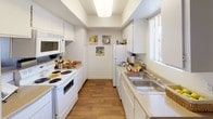 This single-floor residence offers a thoughtfully laid-out interior with a variety of functional and comfortable living spaces. The galley-style kitchen is efficiently designed with white cabinetry lining both walls, a double-basin sink, a full suite of white appliances including a range and overhead microwave, and warm wood-look flooring that runs underfoot. A window at the end of the kitchen brings in natural light, brightening the workspace throughout the day.

The open living and dining area flows naturally together, featuring wood-look flooring, a textured ceiling, and a ceiling fan overhead. The living room provides a relaxed atmosphere, while the adjacent dining space accommodates a table and chairs with ease.

The bedrooms are carpeted and well-sized, each offering natural light through windows dressed with curtains or vertical blinds. The primary bedroom is notably spacious, featuring dual sliding closet doors that reveal generous wardrobe space alongside built-in shelving for additional storage.

The bathrooms are clean and practical. A hallway bathroom includes a tiled shower-tub combination, while a second vanity area with built-in shelving and wood-look flooring provides convenient access to the primary bedroom. Throughout the residence, a neutral color palette and consistent finishes create a cohesive and inviting atmosphere.