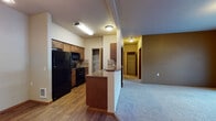 Located at 15720 East 4th Avenue in Spokane Valley, Washington, Unit I103 is a thoughtfully designed single-floor residence that balances comfort and functionality. The open-concept layout connects the kitchen and living areas seamlessly, creating a welcoming and practical flow throughout the space. The kitchen is equipped with black appliances, including a full-size refrigerator, electric range, and over-the-range microwave, complemented by warm wood cabinetry, granite-style countertops, and a tile backsplash. A raised breakfast bar peninsula provides a natural division between the kitchen and the carpeted living area. The spacious living room offers access to a private patio through a sliding glass door with vertical blinds, bringing in natural light. A dedicated closet space houses an in-unit washer, adding convenience to daily living. The bedroom is a comfortable, carpeted room featuring a large window with blinds that allows ample natural light and includes a baseboard heating unit. The bathroom features wood-look flooring, a generous vanity with granite-style countertops, dark wood cabinetry, a wide mirror, and a tub/shower combination. A hallway lined with wood-tone doors connects the various rooms, providing a cohesive and organized layout throughout the unit.