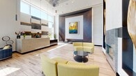 Located at 2827 Telek Place in Alexandria, Virginia, this single-floor office suite at The Point Eisenhower delivers a polished, contemporary work environment designed to impress. The space opens into a dramatic lobby distinguished by soaring double-height ceilings, floor-to-ceiling glass walls, and large-format tile flooring that floods the interior with natural light. A sleek reception desk anchors the lobby, framed by curated artwork, sculptural accents, and a striking wood-paneled feature wall. Vibrant chartreuse and plaid upholstered seating arrangements create inviting areas for visitors and informal collaboration. Glass-partitioned interior offices and a conference room maintain visual openness while offering privacy, with etched geometric patterns on the glazing adding a refined design detail. Patterned carpeting in the inner corridors and workspaces provides a warm contrast to the hard-surface lobby flooring. A decorative metal grid partition elegantly divides zones without sacrificing transparency. Throughout the suite, bold colors, contemporary furnishings, and abundant natural light from exterior-facing windows combine to create a bright, professional, and visually dynamic atmosphere well-suited for a modern business environment.