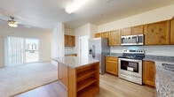 Located along US-34 in Greeley, Colorado, this single-story unit offers a thoughtfully designed layout with a neutral color palette and durable finishes throughout. The kitchen serves as a central highlight, featuring warm honey-toned wood cabinetry extending to the upper walls, granite countertops, and a full suite of stainless steel appliances including a French door refrigerator with ice maker, electric range, over-the-range microwave, and dishwasher. A freestanding kitchen island with open shelving below and a matching granite top provides additional prep space and storage, while light wood-style flooring anchors the area and extends into adjacent spaces.

The living area is generously proportioned with plush carpeting, elevated ceilings, a ceiling fan, and a sliding glass door that invites natural light and outdoor access. Bedrooms are carpeted and well-lit, with large windows fitted with blinds. The bathroom includes a wood-toned vanity with a granite-style countertop, a full tub and shower surround with built-in shelving, and wood-style flooring. The overall ambiance is clean, functional, and welcoming.