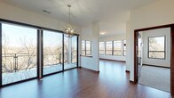 This single-floor residence offers a thoughtfully designed layout with contemporary finishes throughout. The open living and dining area immediately impresses with rich hardwood-style flooring, a striking spherical chandelier, and floor-to-ceiling sliding glass doors that open onto a private balcony overlooking a wooded outdoor setting. Multiple black-framed windows flood the space with natural light, creating a bright and airy atmosphere.

A dedicated living room features plush carpeting, a sleek built-in fireplace with a warm wood mantel, and additional windows offering treetop views. The kitchen is well-equipped with rich wood cabinetry, dark granite countertops, stainless steel appliances including a refrigerator, range, and microwave, and a large window providing ample natural light.

The unit includes two bathrooms—one with a tub-shower combination and wood-toned vanity cabinetry with granite countertops, and a second with a matching vanity and tile flooring. An additional bedroom features hardwood-style floors and an adjoining en-suite bathroom. A generously sized walk-in closet provides extensive wire shelving for organized storage. In-unit laundry with a full-size washer and dryer adds everyday convenience.
