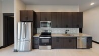 Located at 401 W Kingston Ave in Charlotte's South End neighborhood, this single-floor residence offers a thoughtfully designed modern interior with a cohesive aesthetic throughout. Light wood-style flooring, neutral warm-toned walls, and bold dark baseboards create a clean, contemporary contrast that flows seamlessly from room to room.

The kitchen is a standout feature, showcasing floor-to-ceiling dark espresso cabinetry with sleek hardware, granite countertops, a white hexagonal tile backsplash, and a full suite of stainless steel appliances including a refrigerator, range, and microwave. A peninsula with additional counter space adds functionality and opens the kitchen toward the living area.

The living and bedroom spaces are bright and airy, each benefiting from large windows fitted with roller shades that allow for ample natural light and views of the surrounding Charlotte streetscape. Ceiling fans are present throughout, enhancing comfort and circulation.

The bathrooms are elegantly appointed, featuring granite-topped dark wood vanities, framed mirrors, wall-mounted cabinetry, and striking black hexagonal tile in the tub/shower surrounds. Matte black fixtures add a refined, modern touch. A walk-in closet with built-in wire shelving provides generous storage adjacent to the primary bath, completing the well-appointed layout.