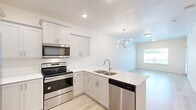 Located at 231 W 12th St in Ogden, Utah, this thoughtfully designed one-bedroom, one-bathroom residence offers a comfortable and functional single-floor layout. The open-concept kitchen and living area serves as the heart of the home, with light wood-style flooring, bright white walls, and natural light streaming through large windows. The kitchen is equipped with stainless steel appliances — including a refrigerator, electric range, microwave, and dishwasher — complemented by white shaker cabinetry, quartz countertops, and a deep double-basin sink set into a peninsula. The living area provides a clean, airy atmosphere ideal for relaxing or entertaining. The generously sized primary bedroom features plush carpeting, a tray ceiling detail, and sliding glass doors that open to a private balcony overlooking greenery. The full bathroom is finished with light tile flooring, white cabinetry with brushed gold hardware, a wide vanity with a large mirror, and a tub-shower combination. A dedicated laundry area with a full-size washer and dryer adds everyday convenience. The overall aesthetic is bright, clean, and modern throughout.