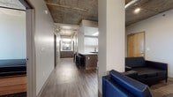 Located at 1031 14th St in the heart of downtown Denver, CO, this modern unit blends industrial design with contemporary finishes throughout its single-floor layout. Exposed concrete ceilings with visible ductwork lend an urban, loft-inspired character to the space, complemented by durable wood-look luxury vinyl plank flooring that runs consistently through the common areas and bedrooms.

The well-appointed kitchen features two-tone cabinetry — dark gray lower cabinets paired with crisp white upper cabinets — alongside white quartz countertops, a subway tile backsplash, stainless steel appliances including a dishwasher and range, and a functional island with bar seating, ideal for casual dining.

A central hallway connects multiple private bedrooms, each furnished with a bed with built-in storage drawers and a dedicated study desk with shelving. Select bedrooms offer windows with views of the surrounding Denver skyline, allowing natural light to filter in.

The shared vanity area features a dual-sink setup with white quartz countertops, dark gray cabinetry, matte black fixtures, and a decorative patterned tile backsplash with mirrored panels. A full bathroom includes a soaking tub/shower combination with built-in shelving. The living area provides comfortable seating, completing this functional and stylish urban unit.
