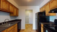 Located at 650 John R Rd in Troy, Michigan, this single-floor unit offers a practical and well-organized layout. The galley-style kitchen is equipped with black appliances, including a refrigerator, dishwasher, and range, complemented by warm oak cabinetry and dark countertops. Tile flooring runs throughout the kitchen, which connects directly to the entry area via a doorway. The living area features neutral-toned carpet and a window with vertical blinds, allowing natural light to fill the space. Bedrooms are carpeted and painted in warm beige tones, each with window treatments and closet access. One bedroom includes a spacious walk-in closet outfitted with dual shelving on opposing walls, providing generous storage. A full bathroom is accessible from the hallway and features an oak vanity, tiled flooring, and a shower-tub combination. An additional bathroom includes wood-style flooring, an extended vanity with a light countertop, and a large mirror. The overall layout, as shown in the 3D model, is efficient and cohesive, with clear circulation between the kitchen, living, and sleeping areas.