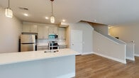 Located at 65 S. Washington Ave in Columbus, Ohio, this two-floor residence offers a thoughtfully designed layout with modern finishes throughout. The main level features an open-concept living and dining area bathed in natural light from large windows, with warm wood-look flooring that flows seamlessly from room to room. The kitchen is a standout, showcasing a large center island with quartz countertops, gray shaker-style cabinetry, a classic white subway tile backsplash, and a full suite of stainless steel appliances including a range, over-the-range microwave, and refrigerator. Pendant lighting above the island adds a refined touch. A half bathroom on the main level is appointed with a gray vanity, white countertop, and a framed mirror with contemporary lighting. The staircase leads to the upper floor, where carpeted bedrooms provide comfort and quiet. One bedroom features a bay-style window arrangement offering pleasant outdoor views and generous natural light. A walk-in closet with wire shelving provides practical storage. The full bathroom upstairs includes a tub-shower combination with white tile surround, a gray vanity with quartz countertop, and wood-look flooring. The upper landing offers an open view to the lower level, enhancing the sense of spaciousness throughout.