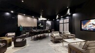 Located at 1435 Fox St in Denver's vibrant 80204 corridor, this single-floor lounge is a masterclass in moody, upscale design. The space is unified by an all-black palette — from the lacquered ceiling to the dark paneled walls — creating a rich, intimate atmosphere punctuated by recessed spotlighting that highlights key architectural moments throughout.

A textured gold mosaic accent wall anchors the wet bar area, which features a sleek dark marble countertop, brass fixtures, and bar seating with bronze-legged stools. Adjacent to the bar, a built-in banquette with plush cushions and a round dining table offer a cozy nook for more intimate gatherings.

The main lounge area is furnished with plush velvet seating arrangements in warm gray tones, complete with brass-framed chairs and a marble coffee table, all set atop layered area rugs over large-format gray tile flooring. A wall-mounted flat-screen display serves as a focal point for this seating zone, with decorative metallic wall accents nearby adding visual interest.

A secondary lounge nook features curved dark leather club chairs arranged around a brass accent table, accompanied by abstract mountain artwork that reinforces the Colorado aesthetic. Striped drapery panels and tall framed windows add softness to the otherwise bold interior, completing this distinctly curated and versatile gathering space.