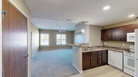 Located in Cedar Rapids, Iowa, this single-floor unit offers a thoughtfully designed layout with a clean, modern aesthetic. The open-concept living and kitchen area serves as the heart of the space, where light-toned carpet flows through the expansive living room, complemented by neutral beige walls and a ceiling fan overhead. Multiple windows allow natural light to fill the room, offering views of the surrounding neighborhood. The kitchen features rich dark-stained cabinetry, granite-style countertops, a peninsula with pendant lighting, a double sink, and a full-size refrigerator. Light hardwood-style flooring in the kitchen and entry area provides a practical contrast to the plush carpet elsewhere. The entryway includes convenient closet access alongside the front door. Bedrooms are generously sized, each finished with soft carpet, warm neutral paint tones, ceiling fans, and wood-paneled interior doors with sleek hardware. Several bedrooms benefit from multiple windows, enhancing natural light and airflow. The bathroom includes a vanity with a white basin sink, dark wood cabinetry, and tile flooring. Throughout the unit, consistent design elements such as recessed lighting, textured ceilings in select areas, and clean white trim create a cohesive and welcoming atmosphere.