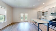 Located at 2829 SW Fairlawn Rd in Topeka, Kansas, this single-floor space showcases a clean, modern design with an open and airy layout. The living area is bright and welcoming, featuring light wood-tone flooring throughout and recessed lighting that enhances the crisp white walls. A set of French doors with a balcony railing floods the living space with natural light and provides a pleasant outdoor view.

The kitchen is a standout feature, outfitted with soft gray shaker-style cabinetry, warm wood open shelving, and a classic white subway tile backsplash. Stone-look countertops extend across the workspace, complemented by a full suite of stainless steel appliances including a range, microwave, dishwasher, and refrigerator. A large island with a stone top and sleek industrial-style metal base provides additional prep and dining space.

A wide hallway connects the living and kitchen areas to the private spaces, featuring a barn-style sliding door that adds a modern architectural touch. The bathroom is finished with elegant details including a marble-look stone countertop, white shaker vanity, brushed gold fixtures, a full soaking tub with shower, and clean tile flooring. The overall design of the space emphasizes contemporary finishes, functionality, and a cohesive neutral palette throughout.