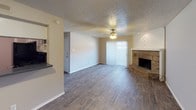 This single-floor residence offers a well-organized layout with consistent wood-look flooring running throughout the main living areas and bedrooms. The living room serves as the heart of the home, highlighted by a brick fireplace with a raised hearth that adds warmth and character to the space. A ceiling fan overhead and sliding glass door with vertical blinds bring in natural light and provide access to the outdoors. Adjacent to the living area, the kitchen is outfitted with white cabinetry extending to the ceiling for ample storage, dark countertops, a mosaic tile backsplash, and a full suite of black appliances including a refrigerator, range, and built-in microwave. The bedrooms are spacious and well-lit, each featuring ceiling fans, textured ceilings, and generous closet space — including walk-in closets with built-in shelving in select rooms. One bedroom features a window seat, adding a charming functional touch. The two bathrooms are clean and practical: one includes a walk-in shower with white tile surround and a dark granite-style vanity countertop, while the other features a full tub-shower combo with white tile walls and overhead cabinetry for additional storage.