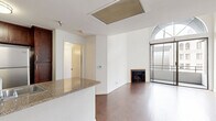 Located at 615 South Kenmore Avenue in the heart of Los Angeles, this well-appointed one-bedroom, two-bathroom residence offers a thoughtfully designed single-level layout. Rich hardwood flooring runs throughout the main living areas, creating a warm and cohesive aesthetic.

The open-concept kitchen and living room form the heart of the home. The kitchen is outfitted with dark espresso cabinetry, granite countertops, a peninsula with a built-in sink, and a full suite of stainless steel appliances including a gas range, microwave, refrigerator, and dishwasher. A ceiling fan in the adjoining living area adds comfort, while built-in shelving provides added storage and display space.

The living room is a standout, featuring a classic fireplace, access to a private balcony, and a dramatic arched floor-to-ceiling window that floods the space with natural light and frames views of the surrounding Los Angeles cityscape.

The bedroom is a comfortable, light-filled retreat with hardwood floors, a large window, and generous proportions. The two bathrooms are finished with granite-topped vanities and dark wood cabinetry, with one featuring a full tub-shower combination with tile surround. A hallway connects the bedroom and bathrooms, enhancing privacy and flow throughout the residence.