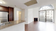 Located at 615 South Kenmore Avenue in the heart of Los Angeles, this well-appointed one-bedroom, two-bathroom residence offers a thoughtfully designed single-level layout. Rich hardwood flooring runs throughout the main living areas, creating a warm and cohesive aesthetic.

The open-concept kitchen and living room form the heart of the home. The kitchen is outfitted with dark espresso cabinetry, granite countertops, a peninsula with a built-in sink, and a full suite of stainless steel appliances including a gas range, microwave, refrigerator, and dishwasher. A ceiling fan in the adjoining living area adds comfort, while built-in shelving provides added storage and display space.

The living room is a standout, featuring a classic fireplace, access to a private balcony, and a dramatic arched floor-to-ceiling window that floods the space with natural light and frames views of the surrounding Los Angeles cityscape.

The bedroom is a comfortable, light-filled retreat with hardwood floors, a large window, and generous proportions. The two bathrooms are finished with granite-topped vanities and dark wood cabinetry, with one featuring a full tub-shower combination with tile surround. A hallway connects the bedroom and bathrooms, enhancing privacy and flow throughout the residence.