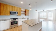 This single-floor space is designed with a clean, modern aesthetic and an open layout that promotes a sense of spaciousness. The kitchen serves as a central highlight, showcasing warm wood-tone upper cabinetry paired with crisp white lower cabinets. Granite countertops extend across the perimeter and onto a central island, which also features pendant lighting above. Stainless steel appliances — including a gas range, built-in microwave, French door refrigerator, and dishwasher — complete the kitchen's contemporary appeal. A white subway tile backsplash adds a polished finishing touch. Light hardwood flooring flows seamlessly throughout the entire space, creating visual continuity.

The living area is bathed in natural light from a large window and glass door, complemented by a ceiling fan. Neutral-toned walls maintain a bright, airy atmosphere throughout.

The bathroom features granite countertops atop white cabinetry, a undermount sink, and a large mirror. It connects directly to a well-organized walk-in closet with built-in shelving and drawers. An in-unit stacked washer and dryer adds everyday convenience, rounding out the practical and thoughtfully designed layout of this space.