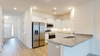 This two-story home is designed with a clean, contemporary aesthetic throughout, combining practical finishes with an open, airy feel. The kitchen serves as a standout space, outfitted with crisp white shaker-style cabinetry, speckled granite countertops, and a full suite of stainless steel appliances including a French door refrigerator with ice maker, electric range, over-the-range microwave, and dishwasher. A peninsula with an undermount sink offers additional prep and seating space, while recessed lighting and light wood-look tile flooring tie the space together seamlessly. The adjacent living area is generously proportioned, featuring the same wood-look flooring, recessed lighting, and a ceiling fan, offering a bright and open atmosphere. A wide hallway with recessed lighting connects the main living areas to the bedrooms, which feature plush carpeting, ceiling fans, and windows that bring in natural light. The bathrooms are well-appointed, with one featuring a dual-sink vanity with white cabinetry and ample counter space, and another offering a similarly clean double-sink layout. A dedicated laundry area houses a full-size Samsung washer and dryer set with overhead wire shelving for storage. Throughout the home, white walls, consistent flooring choices, and thoughtful finishes create a cohesive and move-in-ready environment.