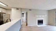 Located at 4901 Tall Timber Dr in Raleigh, NC, this one-bedroom, one-bathroom residence offers a well-designed single-level layout with a neutral color palette and light-toned luxury vinyl plank flooring throughout. The open-concept living and kitchen area serves as the heart of the home, anchored by a white-surround fireplace with a classic mantel and direct access to a private balcony through sliding glass doors that bring in generous natural light. The kitchen is thoughtfully appointed with white shaker cabinetry, a tile backsplash, stainless steel appliances including a range, microwave, and refrigerator, and a white quartz peninsula with an undermount sink — ideal for both meal prep and casual dining. A dedicated in-unit laundry area with a full-size washer and dryer adds everyday convenience. The bedroom offers a comfortable footprint with a large window that fills the room with natural light and provides outdoor views, complemented by closet storage. The full bathroom features a combined tub and shower, a white vanity with quartz countertop, and matte black hardware accents. Textured ceilings, clean white trim, and a cohesive warm-gray finish tie the space together throughout.