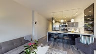 This contemporary single-floor residence at 1224 West Riverside Avenue in Spokane, Washington, offers a thoughtfully designed open-concept layout with modern finishes throughout. The kitchen is a standout feature, showcasing high-gloss dark cabinetry, stainless steel appliances including a French door refrigerator, a mosaic tile backsplash, and a generous marble-top island with bar seating — all illuminated by striking globe pendant lights and track lighting overhead. Glass shelving adds a refined, open display element to the kitchen's design. The living area flows naturally from the kitchen and is anchored by a fireplace set against a bold teal accent wall. Floor-to-ceiling corner windows flood the space with natural light and frame lush treetop views, while a sliding glass door provides access to an outdoor balcony. Light wood-style flooring runs consistently throughout, lending warmth and continuity to the space. A hallway with sleek glass-panel sliding doors leads to the bedroom, which is comfortably proportioned and well-lit. The bathroom is finished with large-format white wall tiles, a frameless glass sliding shower enclosure with a mosaic tile floor, and a clean white vanity with modern fixtures. Track lighting and thoughtful design details are present throughout, reflecting a cohesive, urban aesthetic.