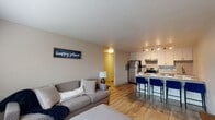 Located at 4926 Sonata Dr in Colorado Springs, CO, this single-floor unit offers a thoughtfully designed open-concept layout that seamlessly connects the living area and kitchen. The living space features warm wood-look flooring, neutral walls, and natural light streaming through blinds-covered windows, creating a bright and welcoming atmosphere. The kitchen is a standout feature, showcasing white cabinetry, granite countertops, stainless steel appliances including a refrigerator, electric range, and dishwasher, along with a geometric-patterned tile backsplash and track lighting overhead. A peninsula with a granite countertop and seating for multiple bar stools provides an ideal casual dining and entertaining space. The bedroom is carpeted for comfort, includes a ceiling fan with light, and benefits from natural light through a window. The bathroom features a tiled tub-shower combo with classic fixtures. Throughout the unit, the design balances modern finishes with a clean, functional aesthetic, making it a practical and comfortable living space in a residential Colorado Springs neighborhood.