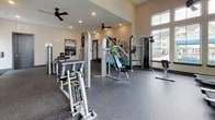 Located at 1001 Linger Longer Dr in Summerville, SC, this single-floor fitness center is designed to support a comprehensive workout experience. The space is generously proportioned, with soaring ceilings and an abundance of large windows that flood the interior with natural light and offer views of the surrounding community. Ceiling fans are distributed throughout, contributing to a comfortable environment during exercise.

The main workout area is outfitted with a strong selection of Inflight Fitness strength machines, including cable stations, leg press, and isolation equipment, all arranged to allow ample space for movement between stations. A dedicated free weights zone features a tiered dumbbell rack stocked with a full range of weights, accompanied by full-length wall mirrors that enhance the sense of space and assist with proper form. Stability balls, resistance bands, medicine balls, and exercise mats are also available, supporting functional and flexibility training.

A separate cardio area houses treadmills, an elliptical, and a stationary bike, positioned beneath large windows with a wall-mounted television for entertainment during workouts. Rubber flooring throughout the facility provides both safety and durability. A motivational "Stronger Than Yesterday" wall graphic reinforces the energetic atmosphere. The layout is thoughtfully organized, offering a well-rounded facility suitable for users of all fitness levels.