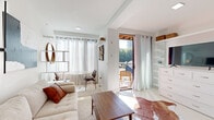 Located at 2936 Summit St in Kansas City, MO, this single-floor unit offers a thoughtfully designed, light-filled interior with a cohesive modern aesthetic. The main living area is open and airy, featuring white walls, light flooring, and an abundance of natural light streaming through sheer floor-to-ceiling curtains. The space is anchored by a neutral tufted sofa, a walnut coffee table, and a cowhide area rug, complemented by bold abstract wall art that adds visual interest. A round dining table with sleek chairs occupies one corner, while a white built-in dresser with a flat-screen television serves as a practical media console along the opposite wall.

A glass door opens directly onto a private balcony with wood-beam ceiling detail and outdoor seating, creating a seamless indoor-outdoor connection with views of the surrounding cityscape. The compact kitchen is efficiently laid out with rich dark wood cabinetry, neutral countertops, stainless steel appliances, an over-range microwave, and an in-unit washer conveniently integrated into the cabinetry. The bathroom features striking marble-style wall tile, a soaking tub, a vanity with mirror, and matte black hardware accents, maintaining the space's clean, contemporary character throughout.