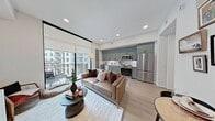This thoughtfully designed 450-square-foot, one-bedroom, one-bathroom apartment at 1120 Town Creek Drive in Austin, Texas, maximizes every inch of its single-floor layout with modern finishes and curated details throughout. The open-concept kitchen and living area serves as the heart of the unit, featuring a sleek galley-style kitchen outfitted with sage-green shaker cabinetry extending to the ceiling, white subway tile backsplash, light quartz countertops, and a full suite of stainless steel appliances including a range, microwave, and dishwasher. Light wood-tone flooring flows seamlessly through the space, complementing the bright, neutral walls. The living area offers views to a private balcony with outdoor access, allowing natural light to pour in. The bedroom spans 90 square feet and features a tall upholstered headboard wall, warm sconce lighting, and a dedicated closet. The bathroom is finished with large-format marble-look tile in the walk-in glass-enclosed shower, mosaic floor tile, and built-in storage cabinetry. A hallway connects the rooms efficiently, completing this compact yet functional floor plan ideal for Austin urban living.