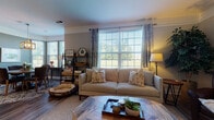 Located at Solomon Square in Delaware, Ohio, this single-floor residence offers a thoughtfully designed layout that balances comfort and functionality. The living room is a welcoming focal point, featuring wide windows that flood the space with natural light, warm hardwood-style flooring, crown molding, and ample room for relaxed seating arrangements. Adjacent to the living area, the dining space impresses with a bold teal accent wall, large windows overlooking greenery, and an elegant geometric pendant light fixture that anchors the room. The kitchen is outfitted with rich dark cabinetry, light countertops, stainless steel appliances including a full-size refrigerator and range, and durable wood-look flooring. The bedrooms offer plush carpeting and generous closet space; one features a textured accent wall adding a sophisticated touch, while another is bright and versatile. Each bathroom is finished with dark vanity cabinetry, light countertops, framed mirrors, and wood-look tile flooring. A walk-in closet with built-in shelving is accessible from one of the bathrooms, providing excellent storage. The overall ambiance throughout is warm, neutral, and move-in ready, with consistent design details that create a cohesive and inviting living environment.