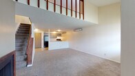Located at 4457 Woodglen St in Kent, Ohio, this two-story home offers a practical and open layout across two levels. The main floor centers around a spacious carpeted living area that opens directly to the kitchen, creating a connected and functional flow. The kitchen is equipped with gray cabinetry, black appliances including a refrigerator and electric range, light countertops, and tile flooring, with a peninsula that separates it from the living space. A closet and additional storage are also accessible on the main level. The vaulted ceiling over the living room adds a sense of height and openness, with an upper-level railing overlooking the space below. The second floor features a loft-style layout with angled ceilings and carpeted flooring, providing a versatile open area bathed in natural light from a window. The upper level also includes a bedroom area with access to a vanity and bathroom, which is fitted with gray cabinetry, a wall mirror with lighted fixtures, and a full tub-shower combination with tile flooring. Textured ceilings are consistent throughout the home, and neutral wall tones create a clean, understated aesthetic across all rooms.