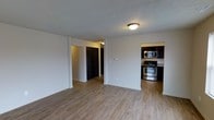 This single-floor residence offers a clean, functional layout with a welcoming open-plan living area as its centerpiece. The space features light-toned hardwood-style flooring throughout, lending warmth and continuity across the rooms. Walls are finished in a crisp white, creating a bright and neutral backdrop that enhances the sense of openness.

The kitchen is accessible directly from the main living area and is outfitted with stainless steel appliances, including a gas range and over-the-range microwave. Dark espresso-toned cabinetry provides a bold contrast against the lighter surroundings, adding a touch of modern style. The kitchen layout appears compact yet efficient, making good use of available space.

From the living area, a hallway leads to additional rooms, including what appears to be a closet or storage space with a dark-paneled door, contributing to the home's practical storage solutions. The textured ceiling adds a subtle architectural detail throughout the unit.

Overall, the space presents a straightforward and practical residential environment with modern finishes, offering a comfortable and move-in ready atmosphere suited for everyday living.