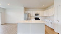 Located at 281 Dorset Ave in Oswego, Illinois, this two-floor home presents a clean, contemporary design characterized by bright white walls, light hardwood-style flooring on the main level, and neutral tones throughout. The open-concept main floor seamlessly connects the living area and kitchen, creating an expansive, airy feel. Large sliding glass doors and multiple windows flood the living space with natural light and provide views of the outdoors. The kitchen is a standout feature, equipped with a generous center island with an undermount sink, white shaker-style cabinetry extending to the ceiling, light quartz countertops, and stainless steel appliances including a gas range, built-in microwave, and French door refrigerator. A dedicated dining area adjacent to the kitchen offers additional versatile space. A bright hallway connects the main living areas to additional rooms, which feature soft carpeting and neutral gray walls. Bathrooms include clean white fixtures with a tub-shower combination. The lower level provides a spacious, carpeted open area with recessed lighting, offering excellent flexibility for a variety of uses. Overall, the home presents a modern, move-in-ready aesthetic with thoughtful finishes throughout.
