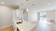 Located at 1800 Silas Deane Highway in Rocky Hill, Connecticut, this well-appointed one-bedroom, one-bathroom unit offers a thoughtfully designed single-floor layout. The open-concept kitchen and living area serves as the heart of the home, featuring light hardwood-style flooring throughout. The kitchen is outfitted with crisp white shaker cabinetry, quartz countertops, stainless steel appliances including a gas range and refrigerator, a stylish kitchen island with an undermount sink and matte black faucet, and pendant lighting overhead. The living area is bathed in natural light and provides direct access to a private outdoor space through sliding glass doors. The spacious bedroom is carpeted for comfort, benefits from generous natural light through a large window, and connects to three closets for ample storage. The full bathroom is finished in a clean, modern aesthetic, showcasing a white vanity with quartz countertop, a backlit mirror, matte black fixtures, and a full tub-shower combination. A dedicated laundry area adds everyday convenience. Neutral tones, clean lines, and quality finishes create a bright and cohesive living environment throughout the unit.