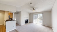 Located at 222 Kyser Blvd in Madison, Alabama, this single-floor residence offers a thoughtfully designed layout with a clean, neutral aesthetic throughout. The spacious living area is a standout, featuring vaulted ceilings, a ceiling fan, a textured ceiling, and a wood-mantled fireplace with built-in shelving on either side. Large sliding glass doors flood the room with natural light and provide direct access to an outdoor space, offering views of the surrounding area. The flooring transitions from wood-look vinyl in the entry areas to plush carpet in the living and bedroom spaces. The kitchen is efficiently designed in a galley style, equipped with warm honey-toned wood cabinetry, dark countertops, stainless steel appliances including a refrigerator, electric range, and microwave, and a peninsula that opens toward the living and dining area. The bedrooms are generously sized, each outfitted with ceiling fans, textured ceilings, and ample natural light from window blinds. At least one bedroom includes a walk-in closet. The bathroom features a tiled tub-shower combination with a classic white tile surround accented by a gray border stripe, complemented by wood-look flooring. Overall, the space presents a functional and comfortable layout well-suited for everyday living.