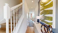 This two-story home is thoughtfully designed to maximize both functionality and style across two distinct levels. The main floor opens into a welcoming hallway with light hardwood-style flooring, recessed lighting, and a classic white staircase with decorative spindles, setting an inviting tone throughout. The open-concept kitchen and living area is a standout feature, showcasing white shaker cabinetry, sleek quartz countertops, a center island with a built-in sink, and a full suite of stainless steel appliances. The adjacent living space is brightened by natural light and a bold accent wall, creating a vibrant yet comfortable gathering area. Upstairs, the three bedrooms offer distinct personalities — the primary bedroom features large sliding glass doors that flood the room with natural light and open to outdoor views of lush green surroundings. The additional bedrooms are well-proportioned, with one styled as a flexible office or guest room with rich green accent walls. Each of the three bathrooms is finished with white cabinetry and clean, modern fixtures. Consistent hardwood-style flooring flows throughout both levels, while crisp white walls and recessed lighting create a bright, cohesive aesthetic across the entire home.