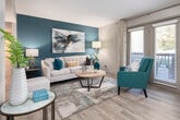 Located at 2954 Columbiana Rd in Vestavia Hills, Alabama, this single-floor residence showcases a thoughtfully designed interior with a cohesive, contemporary aesthetic. The living room serves as the centerpiece of the home, highlighted by a striking teal accent wall adorned with abstract artwork, light wood-style flooring, and large windows with draping curtains that invite abundant natural light. An elegant arched passageway connects the living area to the hallway, adding architectural character to the open layout. The dining area continues the teal color palette with a stylish pendant light fixture, a glass-top table, and a large wood-framed mirror enhancing the sense of space. The kitchen features two-tone cabinetry — white upper cabinets paired with gray lower cabinets — granite-style countertops, and stainless steel appliances including a range, microwave, and dishwasher. The primary bedroom offers dual windows, a ceiling fan, a teal accent wall with coordinating artwork, and light wood flooring, creating a calm and inviting retreat. A second bedroom mirrors this comfortable ambiance with its own ceiling fan and access to a walk-in closet. The bathroom includes granite-topped vanity cabinetry with brushed nickel hardware. Throughout, light wood-style flooring and a consistent teal-and-neutral palette tie each room together cohesively.