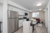 Located in the Hyde Park neighborhood of Los Angeles, this 2-bedroom, 2-bathroom residence offers a thoughtfully organized single-floor layout that maximizes functionality and comfort. The open-plan living, dining, and kitchen area forms the heart of the home, featuring light wood-tone flooring, crisp white shaker cabinetry, stainless steel appliances including a full-size refrigerator, built-in microwave, and range, as well as a dedicated dining space—all bathed in natural light from a street-facing window. The primary bedroom is a spacious retreat with plush carpet flooring, dual windows with blinds, a ceiling fan, wall-mounted TV, and a generous closet. The second bedroom, also carpeted and naturally lit, is versatile enough to serve as a guest room or home office. The two bathrooms include one with a full tub-shower combination and wood-look flooring, and a second more compact bath, both finished in a clean, neutral palette. Additional highlights include multiple closets for ample storage, an in-unit laundry area, and an overall bright, modern aesthetic with white walls and consistent finishes throughout that create a cohesive and welcoming atmosphere.