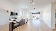 This contemporary single-floor unit showcases a clean, modern design highlighted by light hardwood flooring and crisp white walls throughout. The open-concept layout seamlessly connects the kitchen and living area, creating a bright and airy atmosphere enhanced by recessed lighting and natural light from multiple windows.

The kitchen is well-appointed with a full suite of stainless steel appliances, including a refrigerator, electric range, over-the-range microwave, and dishwasher. Two-tone cabinetry pairs dark wood lower cabinets with white upper cabinets, complemented by white quartz countertops and a subtle tile backsplash. The living area extends to a sliding glass door that opens to an outdoor balcony, offering views of the surrounding neighborhood.

The bedrooms are comfortably sized, each featuring light hardwood floors, large windows that invite natural light, and dedicated closet space. One bedroom includes a ceiling fan and a walk-in closet with built-in shelving, while another features its own sliding glass door access.

The bathrooms are finished in a clean, minimalist style with wood-tone vanities, white quartz countertops, and a combination shower and bathtub. Consistent hardwood-style flooring flows throughout, tying all areas of the unit together in a cohesive, contemporary aesthetic.