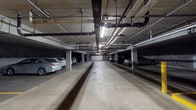 This single-floor commercial space offers a well-appointed and functional layout designed to support professional use. The interior is finished with a drop tile ceiling fitted with recessed fluorescent lighting throughout, neutral-toned walls, and light-colored tile flooring that lends a clean, polished appearance to the common areas.

The kitchen is a standout feature, outfitted with rich dark-stained wood cabinetry extending to the ceiling, granite-look countertops, and a full suite of stainless steel appliances including a refrigerator, electric range, dishwasher, and microwave. A stainless steel backsplash behind the range adds a professional touch, while a double-basin sink with a modern faucet completes the functional workspace. An adjacent breakroom area provides additional counter and cabinet space, along with a large window fitted with horizontal blinds that allows natural light in and offers views of the surrounding neighborhood.

An open corridor connects the kitchen and breakroom to the wider suite, featuring ample wall space that could serve a variety of uses. The space also includes access to an underground parking garage, which provides multiple marked stalls, structural concrete columns, exposed mechanical systems overhead, and a garage door for secure entry and exit.