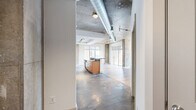 Located at 951 Fell St in Baltimore's vibrant Fell's Point neighborhood, this 2-bedroom, 2-bathroom unit blends industrial character with modern finishes throughout a thoughtfully designed single-floor layout. The open-concept living and kitchen area is the heart of the home, showcasing soaring exposed concrete ceilings with visible ductwork, bold structural columns, and track lighting that highlight the loft-inspired aesthetic. Light hardwood flooring extends through the living space, which opens to a private balcony through floor-to-ceiling sliding glass doors, inviting abundant natural light and outdoor views. The kitchen features warm wood cabinetry, dark granite countertops, stainless steel appliances including a French door refrigerator, and a breakfast bar peninsula beneath a recessed tray ceiling. Both bedrooms are generously proportioned with plush carpet flooring, ceiling fans, and large windows. The primary bedroom includes a walk-in closet with built-in shelving. The bathrooms are finished with slate tile flooring and stone-tiled tub and shower surrounds. The primary bath offers a dual-sink vanity with dark countertops and a large mirror. Additional features include three closets, a utility room, and a hallway connecting the private quarters to the main living areas.