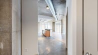 Located at 951 Fell St in Baltimore's vibrant Fell's Point neighborhood, this 2-bedroom, 2-bathroom unit blends industrial character with modern finishes throughout a thoughtfully designed single-floor layout. The open-concept living and kitchen area is the heart of the home, showcasing soaring exposed concrete ceilings with visible ductwork, bold structural columns, and track lighting that highlight the loft-inspired aesthetic. Light hardwood flooring extends through the living space, which opens to a private balcony through floor-to-ceiling sliding glass doors, inviting abundant natural light and outdoor views. The kitchen features warm wood cabinetry, dark granite countertops, stainless steel appliances including a French door refrigerator, and a breakfast bar peninsula beneath a recessed tray ceiling. Both bedrooms are generously proportioned with plush carpet flooring, ceiling fans, and large windows. The primary bedroom includes a walk-in closet with built-in shelving. The bathrooms are finished with slate tile flooring and stone-tiled tub and shower surrounds. The primary bath offers a dual-sink vanity with dark countertops and a large mirror. Additional features include three closets, a utility room, and a hallway connecting the private quarters to the main living areas.