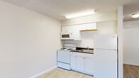 This efficiently designed single-floor unit offers a practical and well-organized layout, incorporating a living area, kitchen, and full bathroom into a cohesive, easy-to-navigate space. Light wood-look plank flooring runs throughout, lending a clean, modern feel that ties the rooms together seamlessly.

The open living area is bright and airy, featuring a large window that brings in natural light and a wall-mounted air conditioning unit for climate control. Neutral-toned walls and a textured ceiling complement the understated aesthetic, providing a versatile backdrop for any décor.

The kitchen is efficiently appointed with white cabinetry offering ample storage, a dark countertop, a double-coil electric range, a built-in microwave, a single-basin sink, and a full-size refrigerator. Flush-mounted overhead lighting ensures the workspace is well-lit. A hallway with a closet connects the main living space to the bathroom and entryway, adding practical storage.

The bathroom is clean and functional, featuring a single-sink vanity with a white cabinet base, a mirrored wall, a standard toilet, and a tiled shower-tub combination with a curtain rod. The same wood-look flooring continues into the bathroom, maintaining visual consistency throughout the unit. Overall, the space is thoughtfully arranged to maximize utility within its compact footprint.