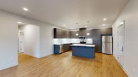 This single-floor residence offers five bedrooms and two full bathrooms within a thoughtfully designed layout. The open-concept kitchen and living area serves as the heart of the home, featuring light bamboo hardwood flooring, recessed lighting, and a seamless flow between spaces. The kitchen is outfitted with floor-to-ceiling gray shaker-style cabinetry, stainless steel appliances including a range, microwave, dishwasher, and refrigerator, along with a striking central island topped with a white marble-style countertop and illuminated by pendant lighting. The living area extends naturally from the kitchen, benefiting from natural light through a sliding glass door. The five bedrooms are finished with plush neutral carpeting and crisp white walls, with several rooms offering windows that bring in natural daylight. A dedicated walk-in closet with wrap-around shelving and hanging rods provides generous storage. The bathrooms feature glass-enclosed showers with brushed nickel fixtures and hardwood-style flooring. A dedicated in-unit laundry room houses a full-size washer and dryer with overhead shelving for added convenience. Three hallways connect the layout efficiently, contributing to a clean and functional flow throughout the home.