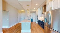 Located at 3015 N Rocky Point Dr E in Tampa, Florida, this thoughtfully designed single-floor residence blends contemporary style with refined finishes throughout. The open-concept kitchen serves as the centerpiece of the space, showcasing a striking two-tone design with crisp white upper cabinetry paired with bold navy lower cabinets accented by gold hardware. A generous waterfall quartz island with an undermount sink anchors the kitchen, illuminated by elegant gold cage pendant lights. The culinary space is equipped with a full suite of stainless steel appliances, including a gas range, double wall ovens, a built-in wine cooler, and a dedicated butler's pantry with a decorative tile backsplash. Warm hardwood flooring flows seamlessly from the kitchen into the expansive living area, where floor-to-ceiling glass windows and sliding doors flood the space with natural light and provide open views of the surrounding Tampa landscape. The bedroom continues the airy, light-filled aesthetic with its own floor-to-ceiling window wall. The primary bathroom features a dual-sink navy vanity with gold fixtures, large-format white tile flooring, and a glass-enclosed shower with marble-style tile surround. An in-unit stacked washer and dryer add everyday convenience to this polished, move-in-ready residence.