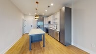 Located at 200 Henry Hill St in Cary, NC, this thoughtfully designed single-floor residence offers a clean, contemporary aesthetic throughout. The open-concept kitchen serves as the heart of the unit, showcasing two-tone cabinetry with crisp white uppers and slate gray lowers, complemented by white quartz countertops and a classic subway tile backsplash. A central island with a white countertop and gold hardware accents provides additional prep and gathering space, illuminated by two striking brass pendant lights overhead. Stainless steel appliances — including a side-by-side refrigerator with ice and water dispenser, a gas range, over-the-range microwave, and dishwasher — complete the kitchen. Warm luxury vinyl plank flooring flows throughout the main living areas, adding continuity and warmth. The bedroom features plush neutral carpeting, clean walls in a soft beige tone, and generous outlets and access panels for convenience. The bathroom is well-appointed with a wide white vanity, gold hardware, a glass-enclosed walk-in shower, and light wood-tone flooring. A walk-in closet adjacent to the bathroom offers dedicated storage space. Completing the unit is a stacked Samsung washer and dryer conveniently integrated into the layout, adding everyday practicality to this modern Cary residence.