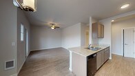 This single-floor unit offers a thoughtfully designed open-concept layout that seamlessly connects the kitchen, dining, and living areas. The kitchen is a functional highlight, featuring a galley-style configuration with warm taupe cabinetry, granite-style countertops, a double stainless steel sink, a dishwasher, a black refrigerator, and a black range. A peninsula with an extended breakfast bar creates a natural boundary between the kitchen and the main living space, adding casual dining and prep space.

The open living and dining area is bright and welcoming, illuminated by a ceiling fan with a built-in light fixture and a stylish multi-pendant chandelier over the dining area. Wood-look flooring runs throughout the main living spaces, adding warmth and continuity. A door with an adjacent window provides access to an outdoor area, bringing in natural light and views.

The bathroom is clean and practical, equipped with granite-style vanity countertops, taupe cabinetry, a well-lit mirror, and a dedicated walk-in shower with chrome fixtures and a built-in shelf. Wood-look tile flooring extends into the bathroom, maintaining a cohesive aesthetic throughout the unit. The overall design is modern, neutral, and move-in ready.