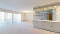 Located at 4601 Glenwood Park Ave in Erie, PA, this single-floor home offers five bedrooms and three full bathrooms across a generously sized layout. The living room serves as the heart of the home, featuring soft carpet flooring, a elegant pendant chandelier, and a striking built-in white display unit with glass shelves, mirrored backing, and integrated lighting — a true standout feature. Large sliding glass doors with vertical blinds invite abundant natural light and provide outdoor views. The spacious primary bedroom includes a wide picture window overlooking mature trees, a baseboard heating system, and plush carpeting. Additional bedrooms offer comfortable dimensions, with one featuring classic striped wallpaper and built-in closet access. The kitchen is outfitted with white cabinetry, light wood-style flooring, and stainless steel appliances including a range, over-the-range microwave, and refrigerator. Three full bathrooms are finished with white tile, white vanities, and glass-enclosed shower stalls. One bathroom features floral wallpaper and gold-tone fixtures, adding a traditional charm. A dedicated hallway and closet provide practical storage solutions. The home maintains a clean, neutral palette throughout, creating a bright and welcoming atmosphere.