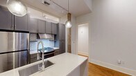 Located at 221 Chartres Street in the heart of New Orleans' historic French Quarter, this thoughtfully designed 3-bedroom, 2-bathroom unit offers a modern living experience within one of the city's most iconic neighborhoods. Warm hardwood floors run throughout, tying together a clean, contemporary aesthetic accented by crisp white walls and tall baseboards.

The kitchen is a standout feature, boasting gray shaker-style cabinetry that extends to the ceiling, stainless steel appliances including a gas range and refrigerator, a herringbone-patterned tile backsplash, and a white quartz peninsula with an undermount sink — all illuminated by stylish pendant lights and a track lighting system.

The three bedrooms are bright and well-proportioned, with recessed lighting and transom-style windows that allow natural light to filter in. The primary bedroom connects to a dedicated closet and a sleek en-suite bathroom featuring a double-sink quartz vanity, large-format tile accents, and modern fixtures. The second bathroom offers a full tub-shower combo clad in classic white subway tile, grey floor tile, and a warm wood-toned vanity.

A private outdoor deck with wood tile flooring and a slatted privacy panel completes the unit, offering a quiet outdoor retreat in the midst of this vibrant urban setting.